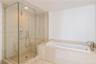 Walk-in glass-enclosed shower with stone-finish tiling and built-in bench, paired with a drop-in soaking tub featuring stone-finish surround and metal