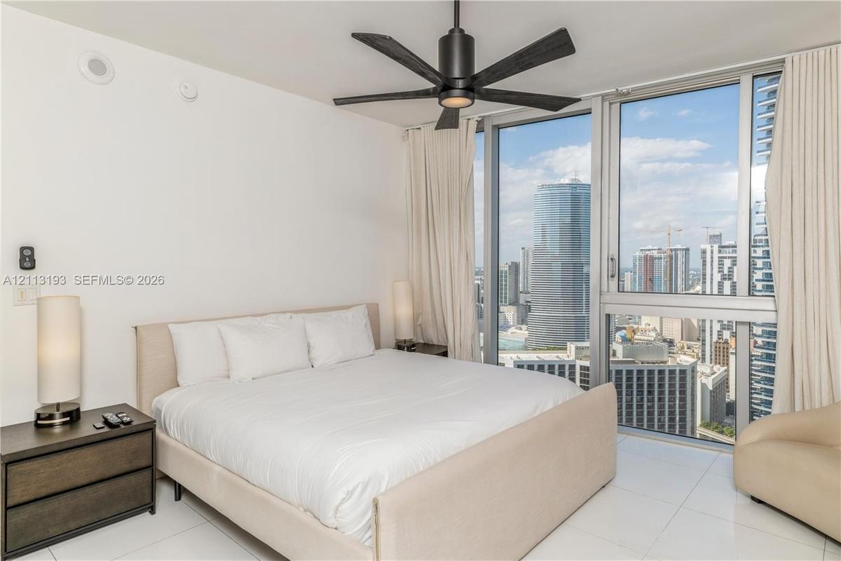 Floor-to-ceiling windows featuring urban skyline scenery, minimalist polished tile flooring, and a contemporary matte black ceiling fan