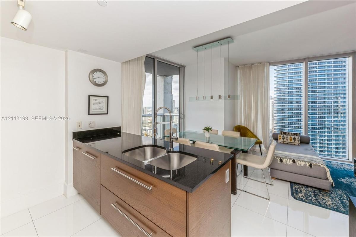 Kitchen island featuring wood-finish cabinetry, dark stone countertops, dual-basin stainless steel sink, and sleek hardware, complemented by large-for