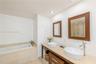 Dual vessel sinks with chrome faucets, stone-topped vanity with wood-finish cabinetry, matching wood-framed mirrors, and a tiled soaking tub