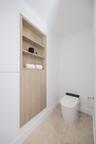 Built-in recessed wood-finish cabinetry featuring open shelving and lower storage cabinets, paired with a modern one-piece toilet and neutral stone-fi