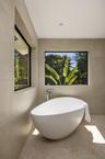 Freestanding soaking tub featuring a chrome floor-mounted faucet, set against large-format neutral tile walls with textured herringbone detailing and 
