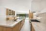 Kitchen featuring light wood-finish cabinetry, natural stone countertops, a large center island, a built-in gas cooktop with pot filler, and glass-fro