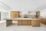 Kitchen featuring custom light wood cabinetry, stone countertops with a waterfall edge island, a built-in range hood, stone backsplash, and recessed l