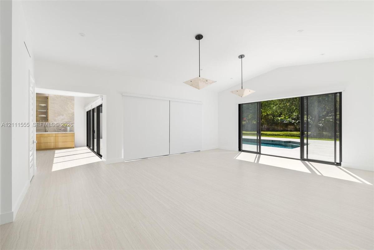 Open living area featuring vaulted ceilings, wood-finish flooring, dual geometric pendant lighting, and multi-panel sliding glass doors with exterior 