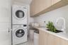 Laundry space featuring stacked front-load laundry appliances, light wood-finish cabinetry, an under-mount sink, white solid-surface countertop, and w