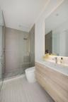 Floating wood-finish vanity with an integrated basin, frameless glass walk-in shower featuring a rainfall showerhead, neutral stone-finish tiling, and