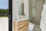 Wall-mounted floating vanity with wood-finish cabinetry, rectangular integrated sink, frameless wall-to-wall mirror, glass-enclosed walk-in shower wit