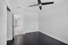 Room featuring dark wood-finish flooring, a multi-blade ceiling fan with integrated lighting, and a solid-core interior door