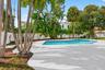 Outdoor space featuring a swimming pool, expansive stone-paver patio, perimeter privacy fencing, and mature palm trees