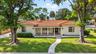 Single-story residence featuring a tile roof, covered front porch, stucco exterior, mature trees, and a manicured lawn
