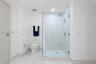 Walk-in glass-enclosed shower featuring stone-finish wall tile, dual-flush elongated toilet, and light-tone wood-finish door