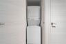Laundry closet featuring a white stacked washer and dryer unit, light wood-finish doors, and brushed metallic hardware