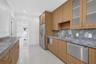 Wood-finish cabinetry featuring glass-front upper cabinets, stainless steel appliances, stone-surface countertops, and high-gloss tile flooring