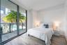 Floor-to-ceiling glass sliding doors, private balcony with metal railing, wood-finish flooring, and neutral wall finishes
