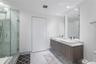 Floating dual-vanity with stone countertop, rectangular vessel sinks, floor-to-ceiling glass-enclosed shower, stone-tile flooring, and full-height wal