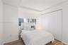 Recessed tray ceiling, horizontal sliding window, and floor-to-ceiling closet with white panel doors, complemented by wood-finish flooring