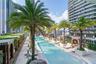 Expansive swimming pool featuring stone deck tiling, built-in wooden cabanas, integrated palm tree planters, and linear pool design