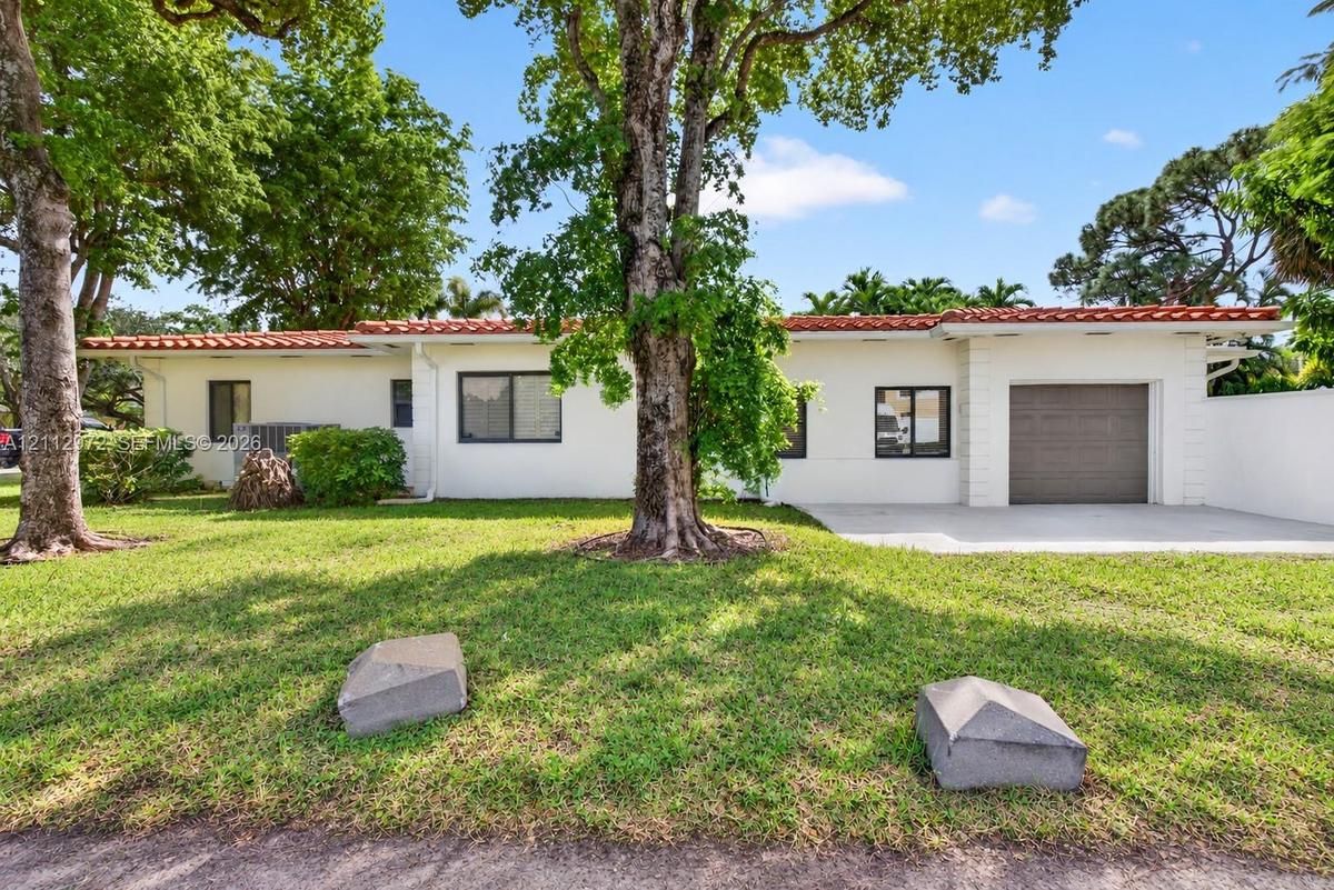 Stucco exterior featuring a terracotta tile roof, single-car garage, and mature trees on a landscaped lot
