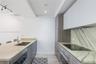 Kitchen featuring stone countertops, stone backsplash, flat-panel wood-finish cabinetry, stainless steel sink with pull-down faucet, and built-in indu