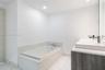 Built-in deep soaking tub with stone-patterned surround, dual-sink vanity with light-tone wood-finish cabinetry, white countertop, recessed lighting, 