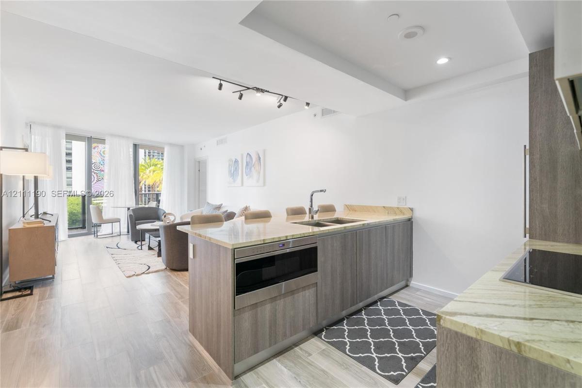 Kitchen featuring an island with a double-basin sink, stone countertops, built-in drawer microwave, and wood-finish cabinetry, complemented by wood-fi