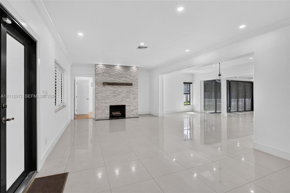 Open-concept interior featuring large-format polished tile flooring, stone-veneer fireplace with a wood mantel, recessed ceiling lighting, and floor-t