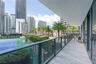 Covered balcony featuring wood-finish tile flooring and a glass panel railing, overlooking a tennis court and urban landscape