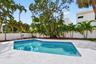 In-ground swimming pool featuring a patterned tile border, concrete deck, solid perimeter wall, and mature palm trees