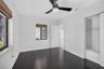 Room featuring dark wood-finish flooring, a contemporary matte black ceiling fan with integrated lighting, two windows with woven shades, and a built-