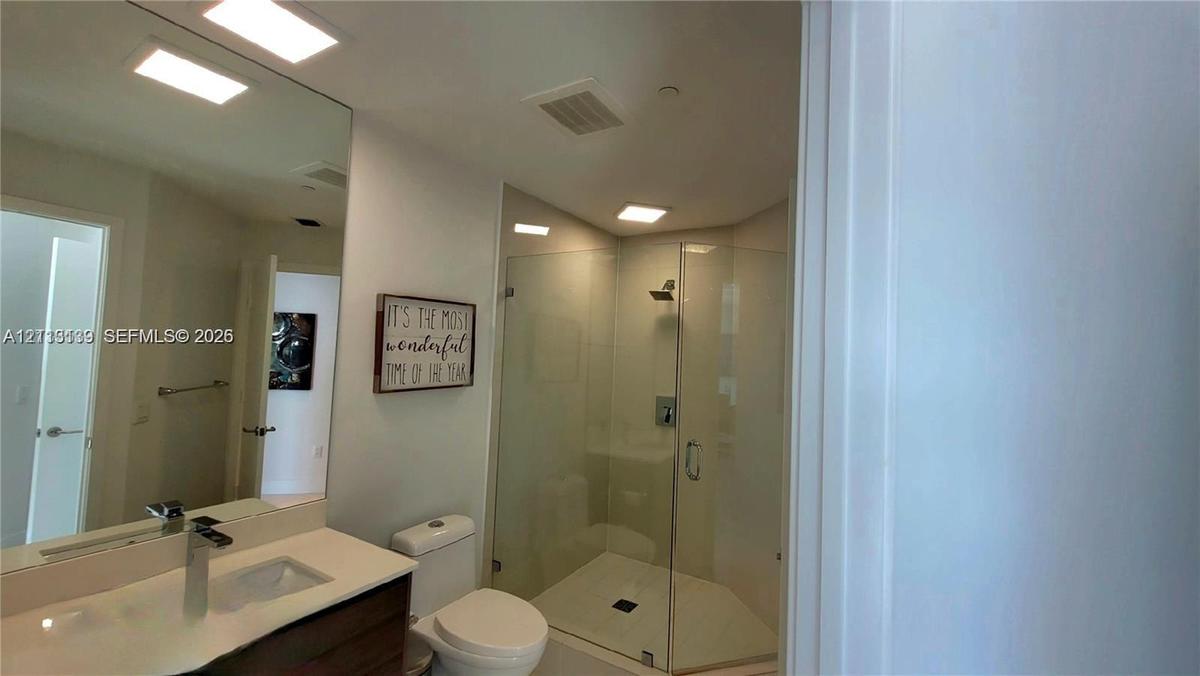 Bathroom featuring a glass-enclosed shower, wood-finish vanity with a rectangular sink, quartz countertop, and a wall-mounted mirror