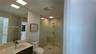 Bathroom featuring a glass-enclosed shower, wood-finish vanity with a rectangular sink, quartz countertop, and a wall-mounted mirror