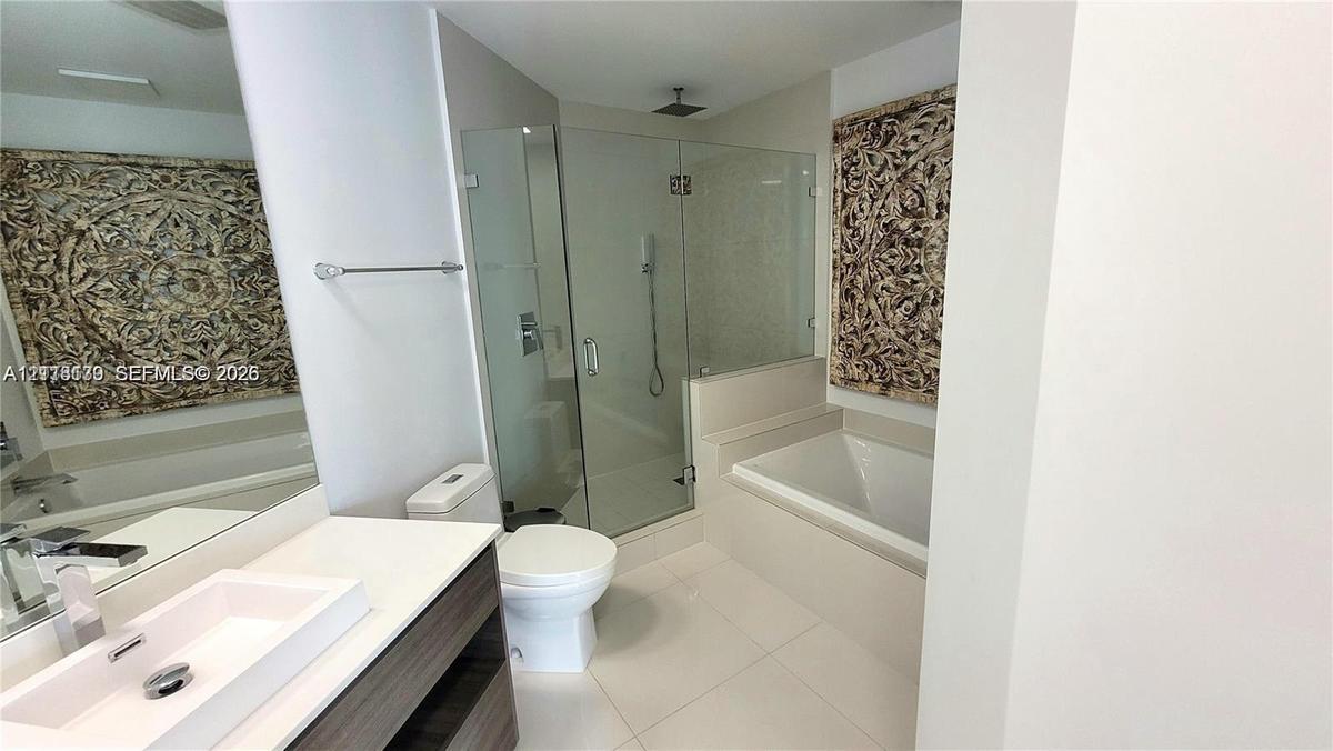 Bathroom featuring a rectangular vessel sink, floating vanity with wood-finish cabinetry, frameless glass-enclosed shower, soaking tub, and large wall