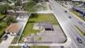 Corner lot featuring a single-story structure with an attached carport, expansive paved surface area, and perimeter chain-link fencing
