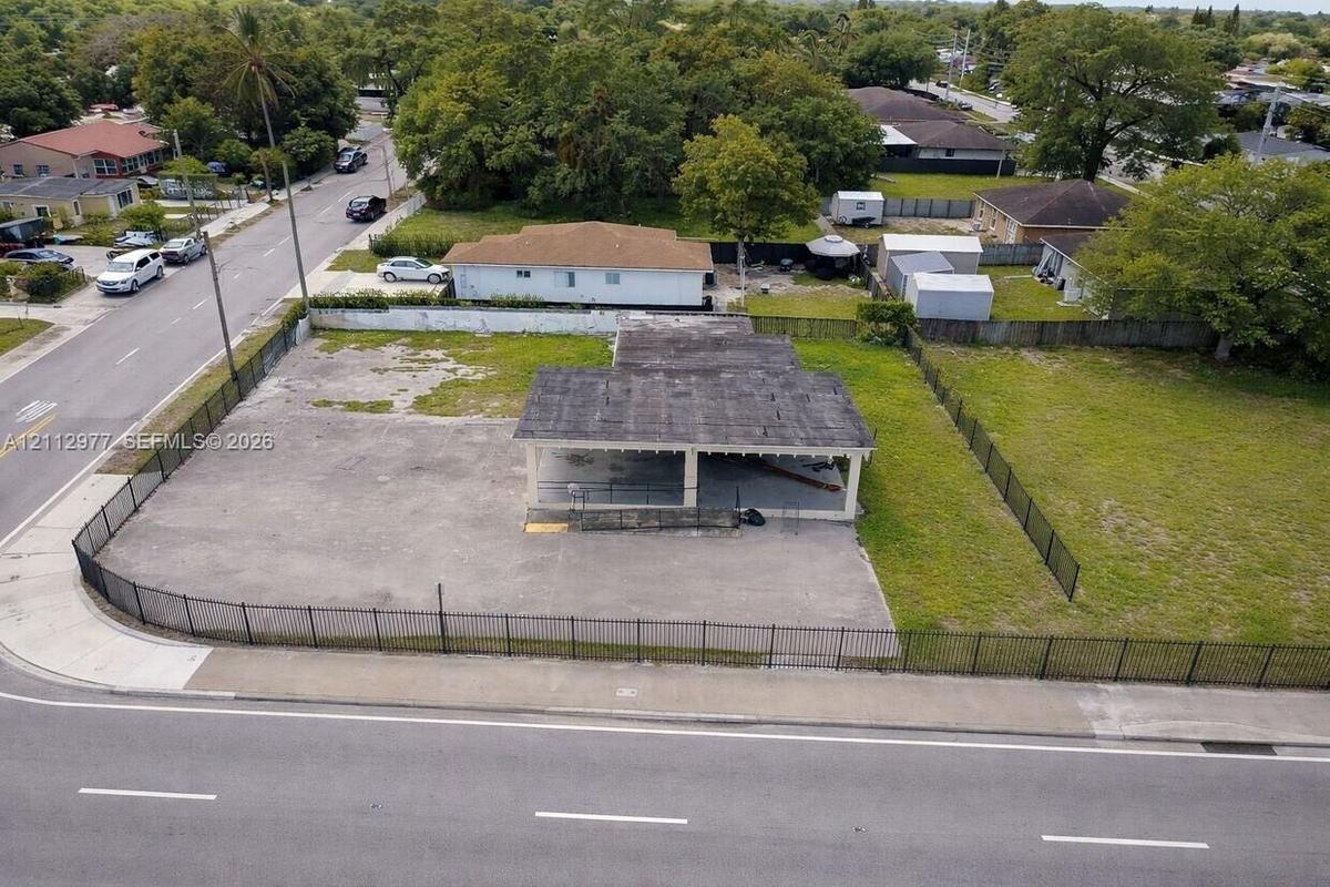 Expansive corner lot featuring a paved surface, structural covered area, and perimeter black metal fencing