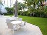 Outdoor patio featuring light-toned stone pavers, expansive green lawn, and mature palm tree landscaping