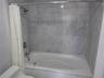 Full-size bathtub with integrated shower, stone tile wall surround, and polished chrome faucet fixtures