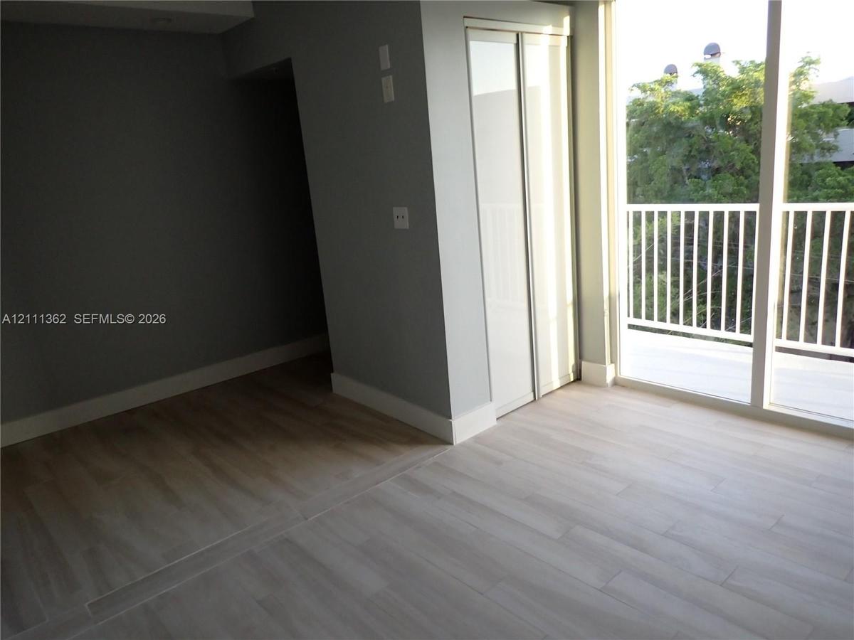 Wood-finish flooring, floor-to-ceiling glass doors, private balcony with white railing, and a reach-in closet with sliding doors
