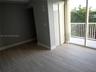 Wood-finish flooring, floor-to-ceiling glass doors, private balcony with white railing, and a reach-in closet with sliding doors