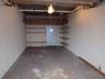 Enclosed garage featuring paved flooring, built-in wooden shelving units, and a dedicated overhead storage platform