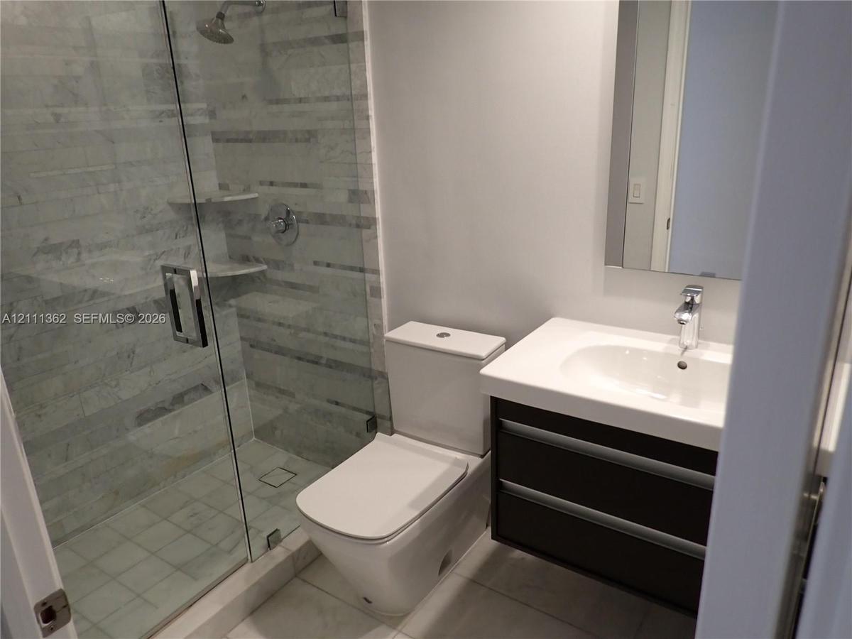 Bathroom featuring a floating vanity with a white countertop, an integrated sink with a chrome faucet, a glass-enclosed shower with horizontal wall ti