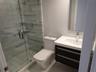 Bathroom featuring a floating vanity with a white countertop, an integrated sink with a chrome faucet, a glass-enclosed shower with horizontal wall ti