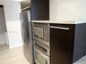 Kitchen featuring dark-finish cabinetry, stainless steel refrigerator, built-in stainless steel microwave and oven, and light-toned stone-finish count