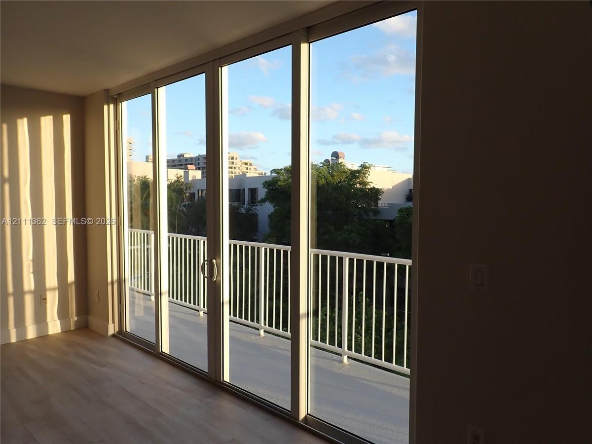 Floor-to-ceiling sliding glass panels, balcony with white metal railing, and wood-finish flooring