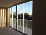 Floor-to-ceiling sliding glass panels, balcony with white metal railing, and wood-finish flooring