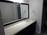 Vanity with stone-finish countertop, integrated oval sink, chrome widespread faucet, and full-width wall mirror with dark wood-finish frame