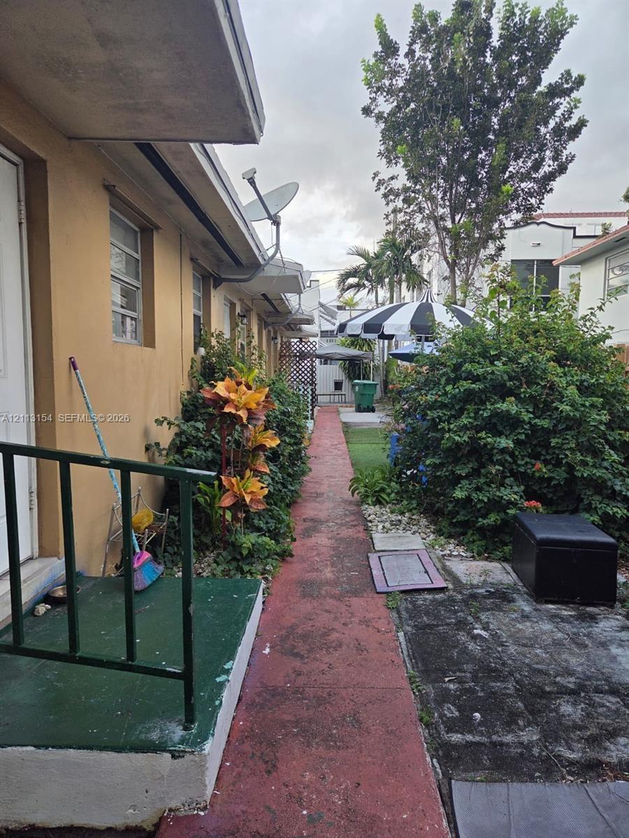 Exterior walkway featuring a concrete path, painted concrete stoops, green metal railings, and mature landscaping