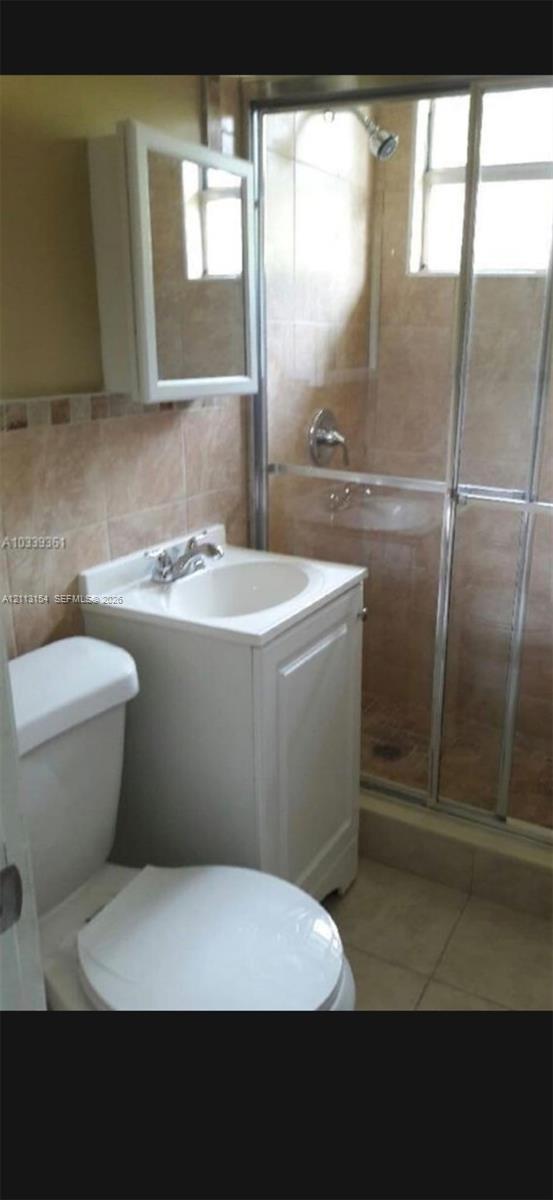 Bathroom featuring a white vanity cabinet with an integrated sink, wall-mounted medicine cabinet, shower enclosure with sliding glass doors, and tiled