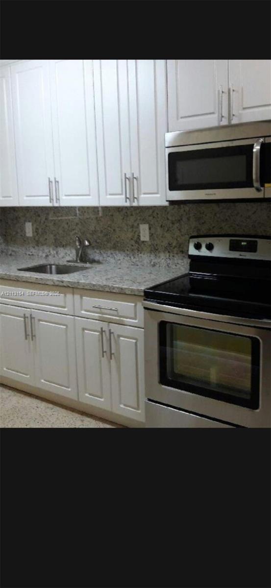 Kitchen featuring white shaker-style cabinetry, stainless steel appliances, stone-patterned countertops, and a stainless steel undermount sink