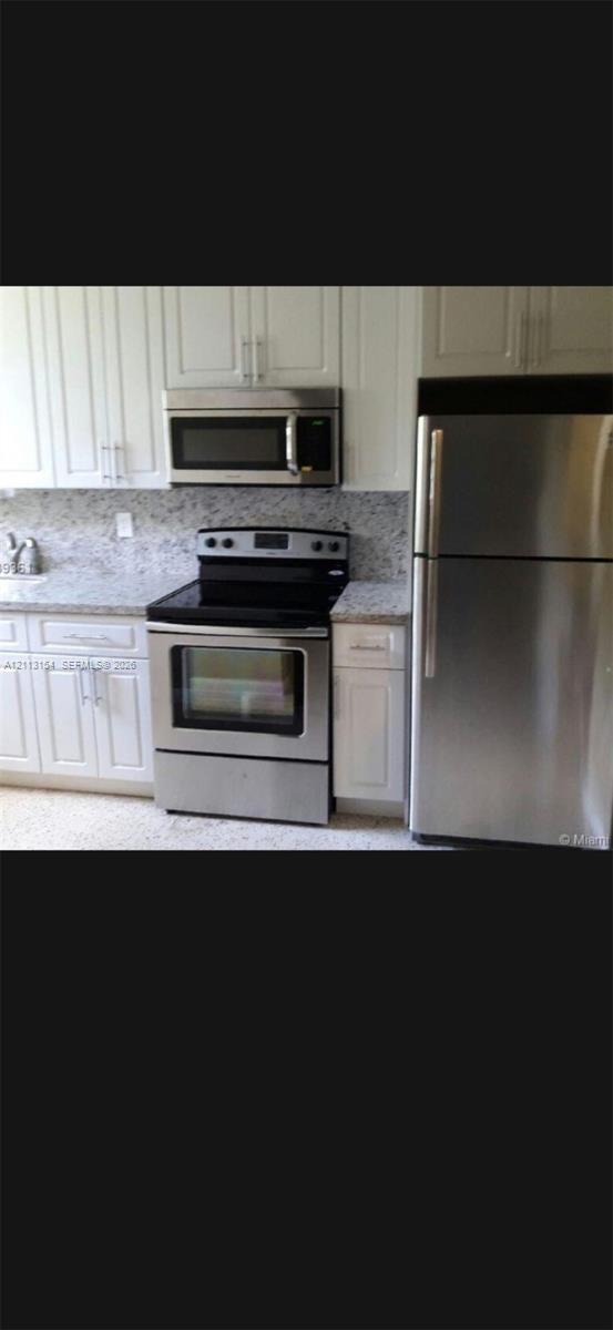 Kitchen featuring white Shaker-style cabinetry, stainless steel appliances, stone-surface countertops, and a stone backsplash